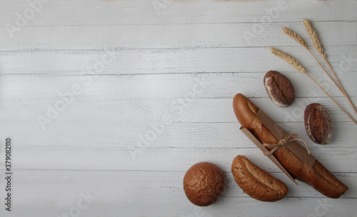 fresh bread - buns, baguette and ears of wheat on wooden background flat lay photo