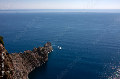 Ship in blue sea and rocky ledge under blue sky