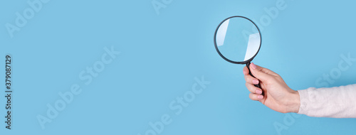 Magnifying glass in hand on a blue background, copy space template, banner.