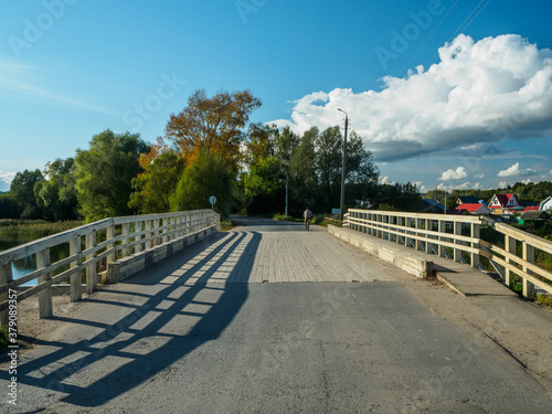 Old wooden road bridge with railings, across the river in the village on a sunny day.