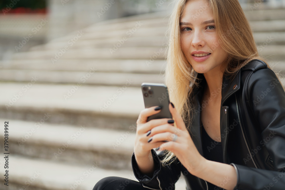 smiling beautiful portrait of a young woman of European appearance. holding the phone in his hands, texting with his best friend about the evening, planning a trip