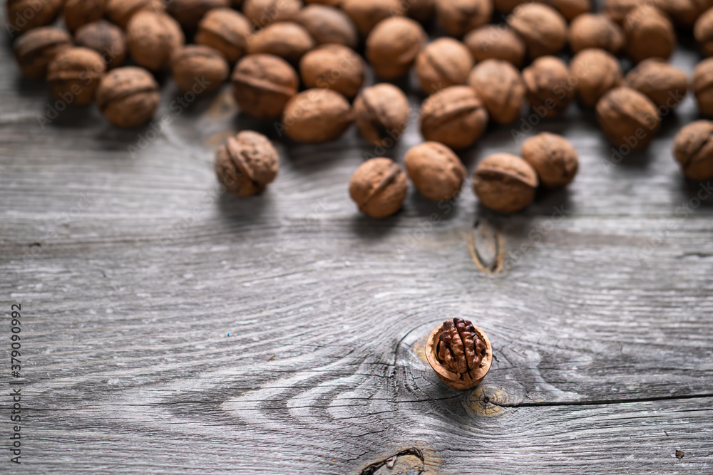 Heap of whole walnuts and one walnut kernel on wooden table - natural pattern background detail. Close up of brown surface texture. Healthy organic food, BIO viands, back to nature concept Heap of whole walnuts and one walnut kernel on wooden table - natural pattern background detail. Close up of brown surface texture. Healthy organic food, BIO viands, back to nature concept