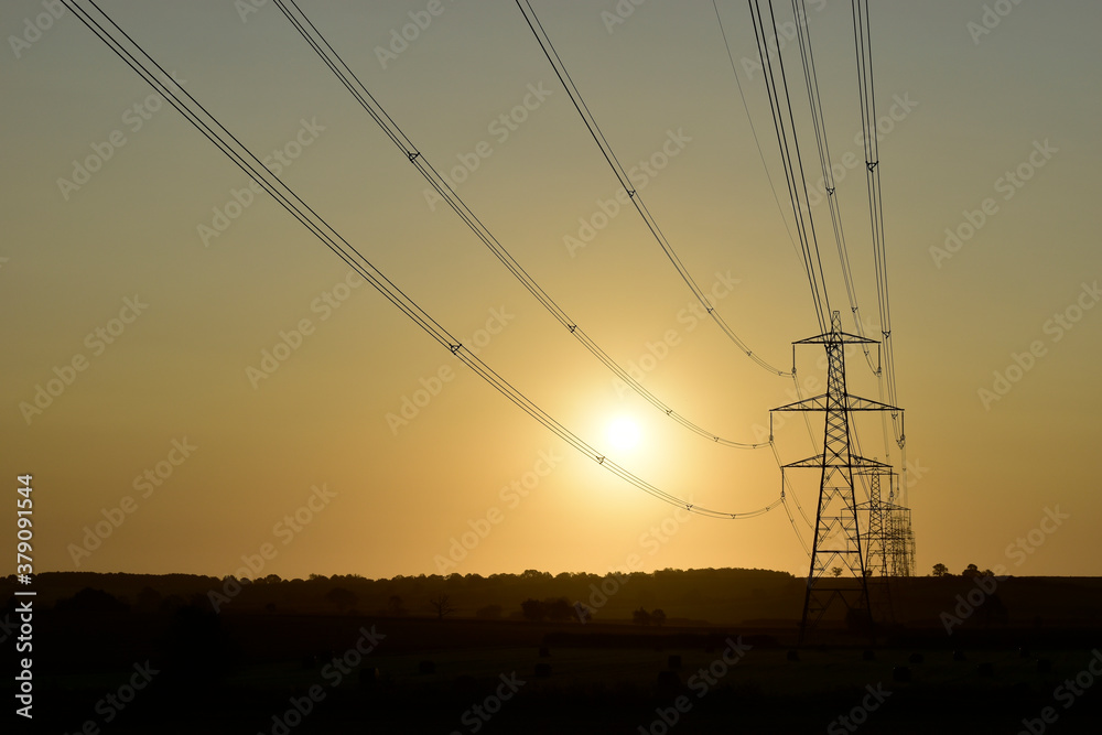 National Grid power lines lead to a row of electricity pylons silhouette at sunrise in Buckinghamshire.