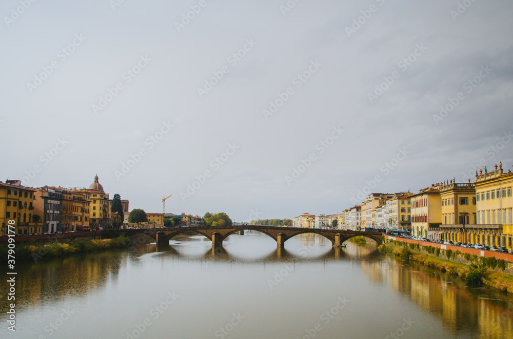 Obraz premium Rome, Italy - A panoramic view of the other side in front of Ponte Vecchio and the Arno river reflecting the buildings in its water during a cloudy afternoon.