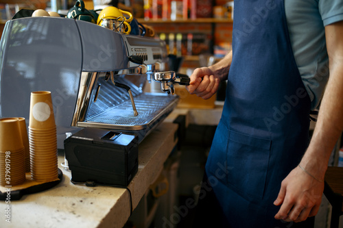 Male barista in apron prepares coffee on machine