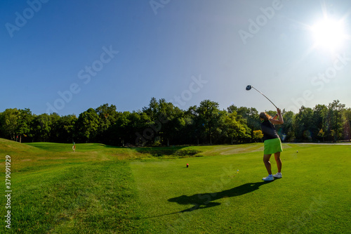 Konstfotografi wide shot female golfer sunny golf course swinging driver on tee