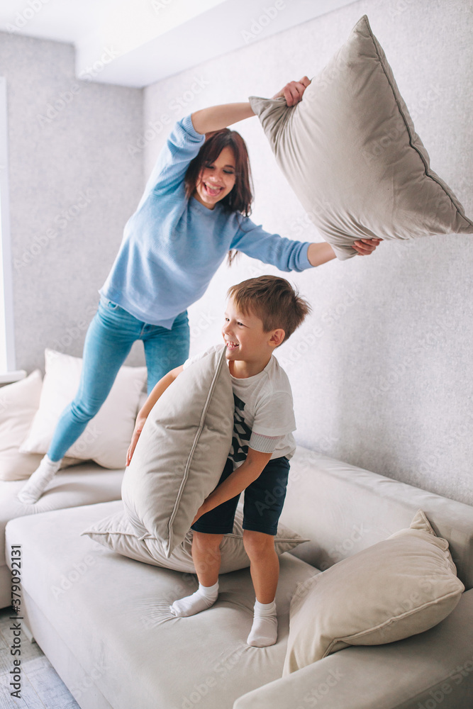 Mother and little son having pillow fight on sofa at home