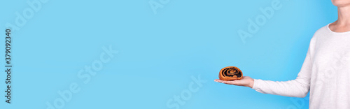 Handmade roll with poppy seed in hand, isolated on blue background, copy space template, banner.