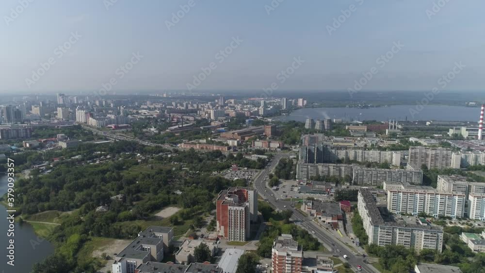 Aerial view of residential city area with old Soviet Russian high-rise houses. Sunny summer day. Behind the houses a pond and a factory. Cars drive through the streets. There are many trees and forest Aerial view of residential city area with old Soviet Russian high-rise houses. Sunny summer day. Behind the houses a pond and a factory. Cars drive through the streets. There are many trees and forest