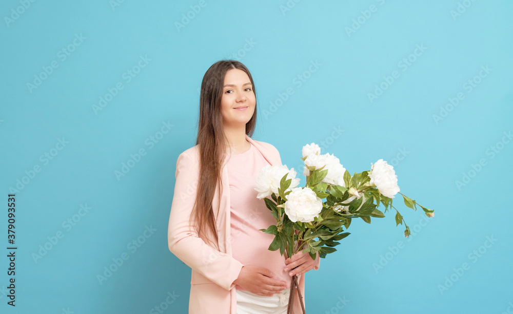 happy young pregnant woman in pink t-shirt on blue background holding a bouquet of flowers