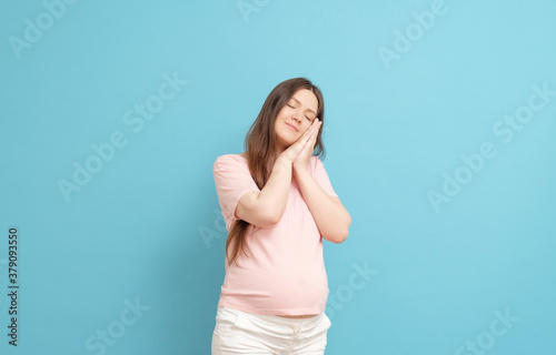sleepy pregnant woman in pink clothes on a blue background © denisval