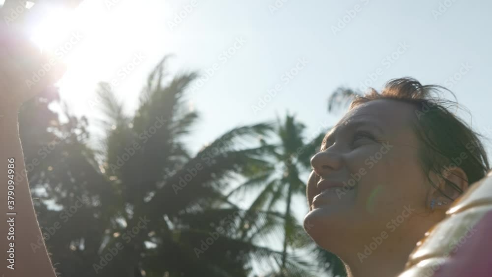 Female Using Black Smartphone on Palm Tree Background. Gadget concept. Reading text message. Waves surface background on sandy beach Female Using Black Smartphone on Palm Tree Background. Gadget concept. Reading text message. Waves surface background on sandy beach