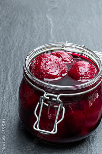 Homemade pickled baby beetroot in glass preserving jar on black stone background