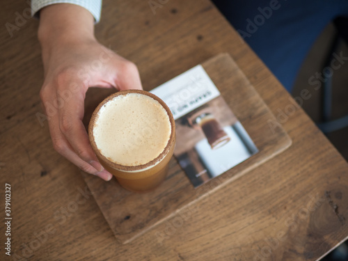 Top view of man's hand hold a glass of coffee on wooden plate in cafe.(Selective focus)