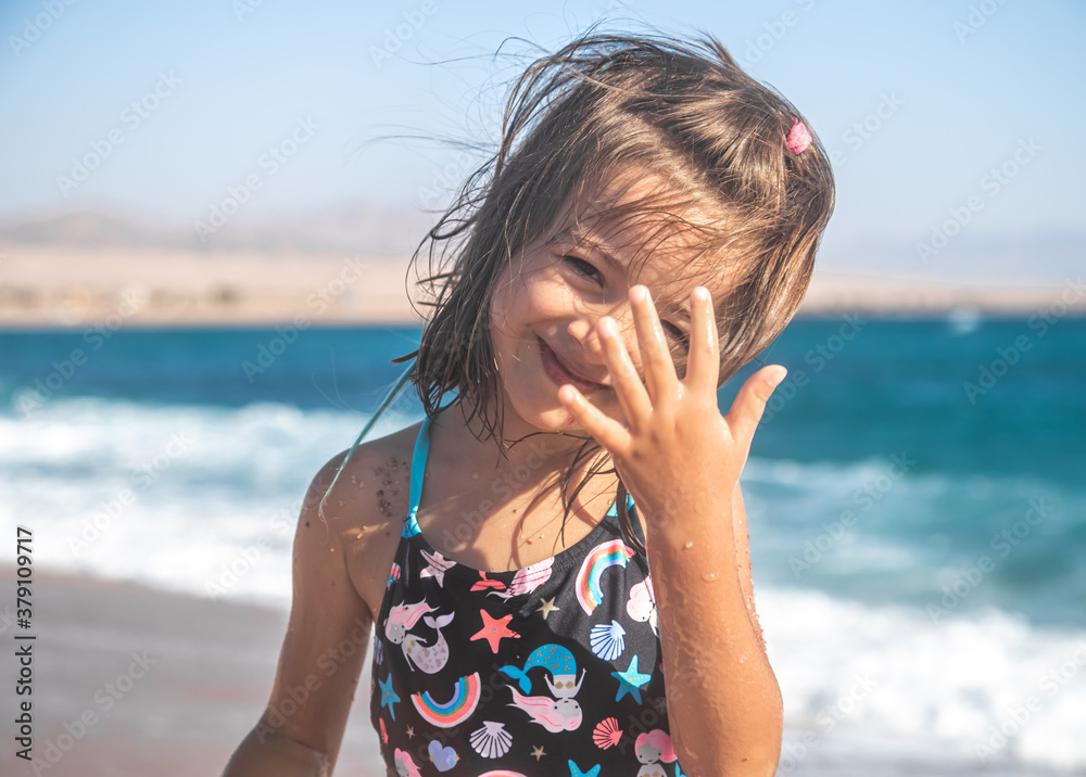 Portrait of a cheerful little girl in a bathing suit by the sea