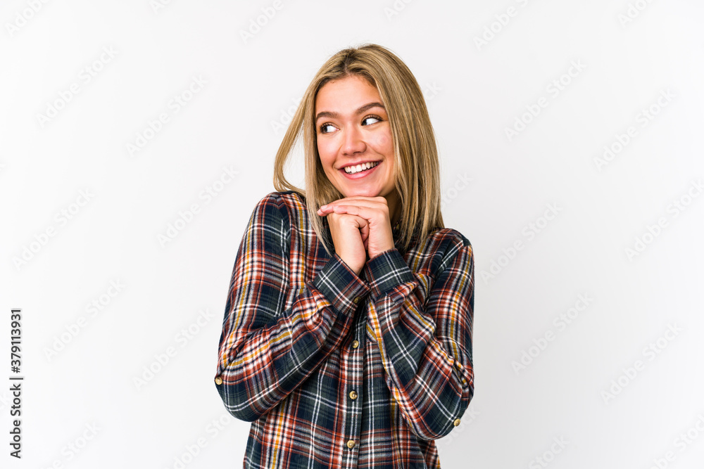 Young blonde caucasian woman isolated keeps hands under chin, is looking happily aside. Young blonde caucasian woman isolated keeps hands under chin, is looking happily aside.