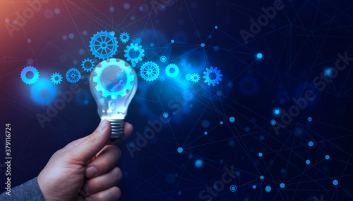 Businessman's Hand Holding Lightbulb With Working Holographic Cogwheels, Blue Background