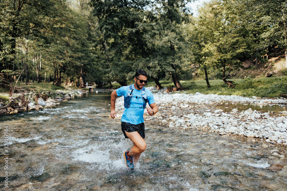 Young adult sporty man fitness and triathlon training in nature. He is running through fresh mountain river. People and extreme sports concept.