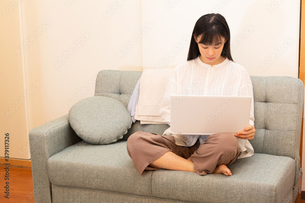 リモートワークで自宅のソファで仕事をする若い女性 リモートワークで自宅のソファで仕事をする若い女性