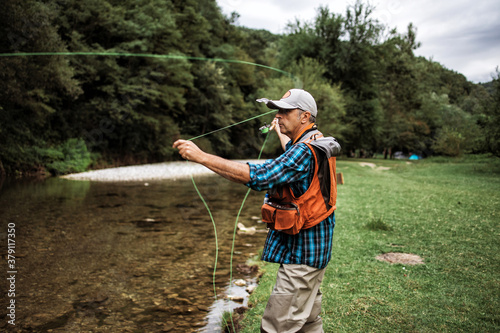 Senior man is fishing alone on fast mountain river. Active people and sport fly fishing concept.