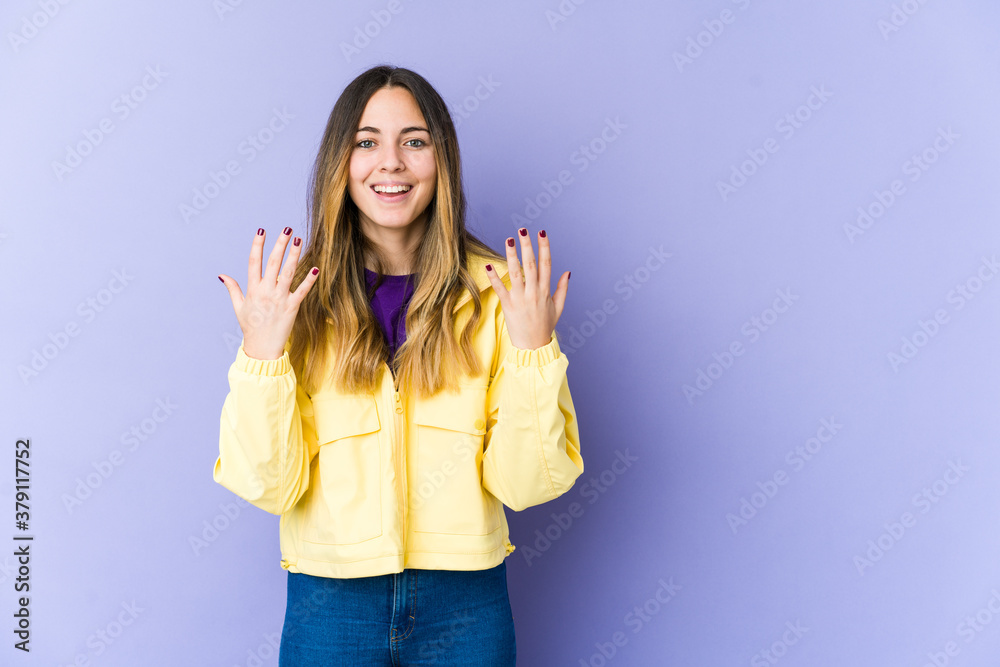 Young caucasian woman isolated on purple background showing number ten with hands.