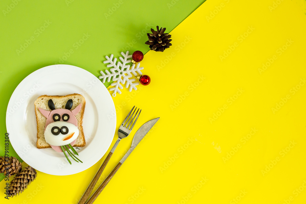 Edible symbol of 2021 year. Creative children's sandwich in the shape of a bull on plate. Cow shaped sandwich with ham, olive, cheese, bread. New year menu. New Year Christmas food top view with copy 