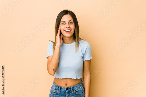 Young woman isolated on beige background shouts loud, keeps eyes opened and hands tense.