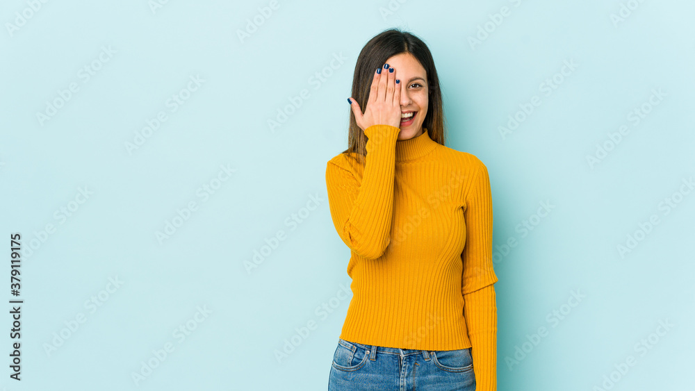 Young woman isolated on blue background having fun covering half of face with palm. Young woman isolated on blue background having fun covering half of face with palm.