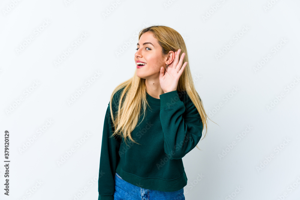 Young blonde woman isolated on white background trying to listening a gossip.