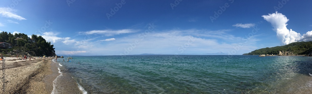 Sunny rock beach in Greece with clody sky with trees on background