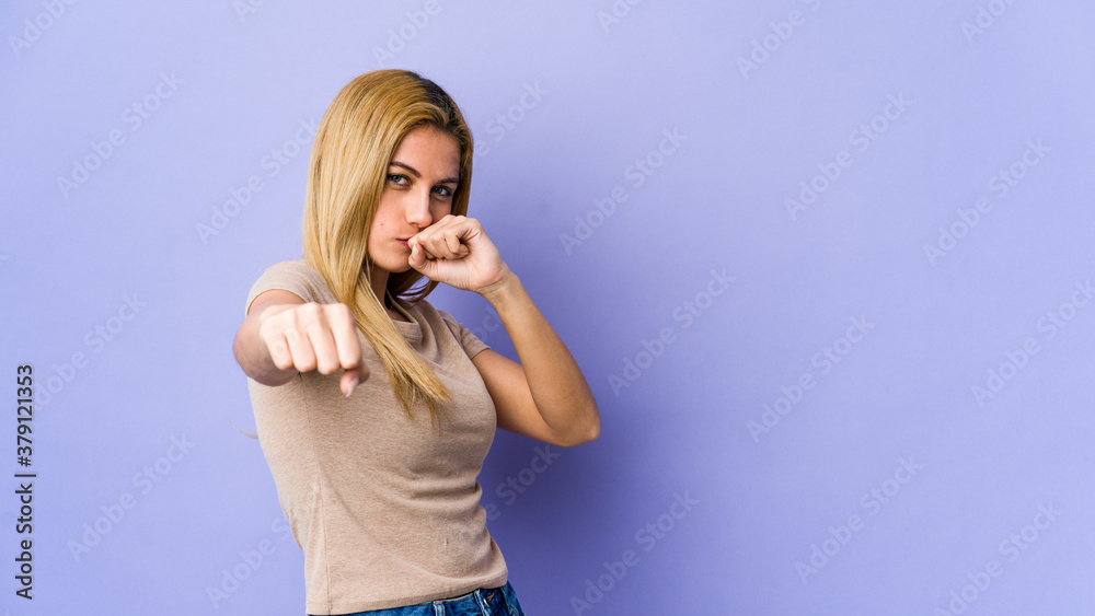 Young blonde woman isolated on purple background throwing a punch, anger, fighting due to an argument, boxing. Young blonde woman isolated on purple background throwing a punch, anger, fighting due to an argument, boxing.