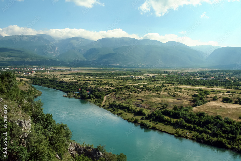 Neretva river in a valley near the city of Mostar (Bosnia and Herzegovina) with mountains and a few clouds in the background, being reflected on the water. Neretva is a major river of Balkans