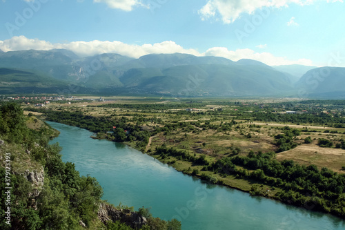 Neretva river in a valley near the city of Mostar (Bosnia and Herzegovina) with mountains and a few clouds in the background, being reflected on the water. Neretva is a major river of Balkans