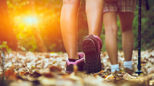 selective focus on trekking shoes, teenagers are hiking and hand holding mountain canes and having soft light.