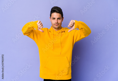 Young caucasian man isolated on purple background showing a dislike gesture, thumbs down. Disagreement concept. © Asier