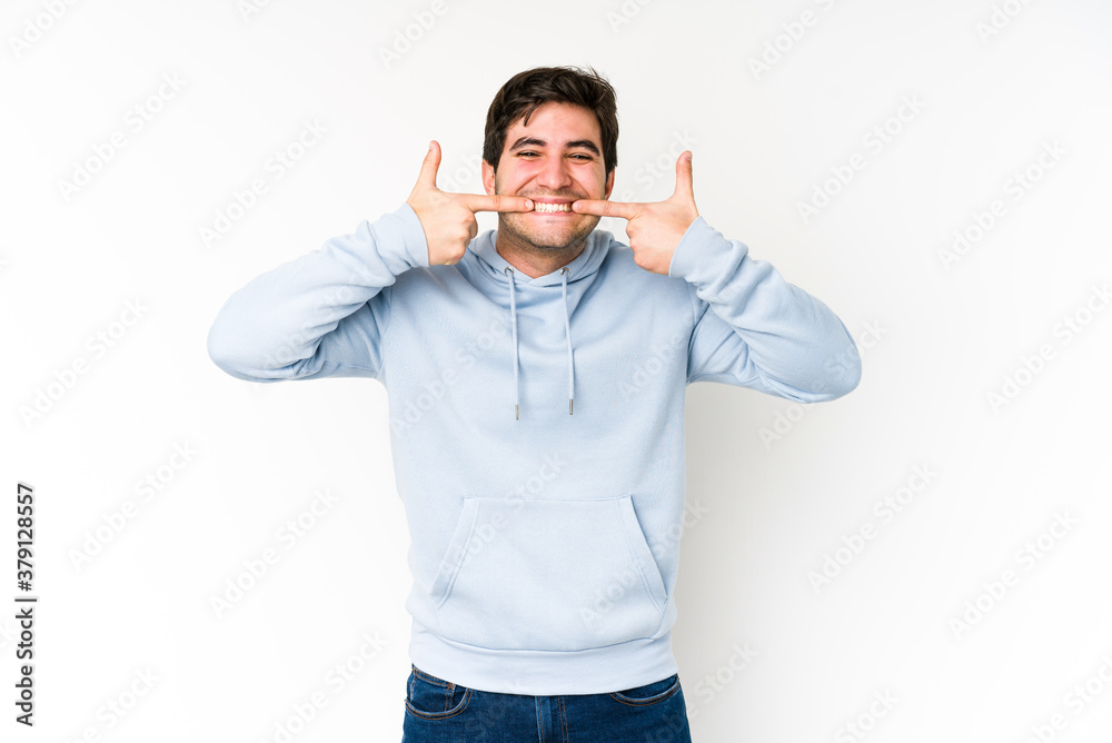 Young man isolated on white background smiles, pointing fingers at mouth. Young man isolated on white background smiles, pointing fingers at mouth.