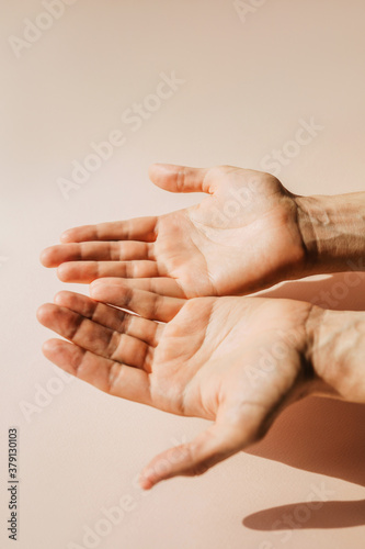 Male hands outstretched forward, palms up on a pink background. photo