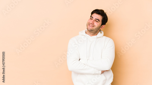 Young man isolated on beige background smiling confident with crossed arms.