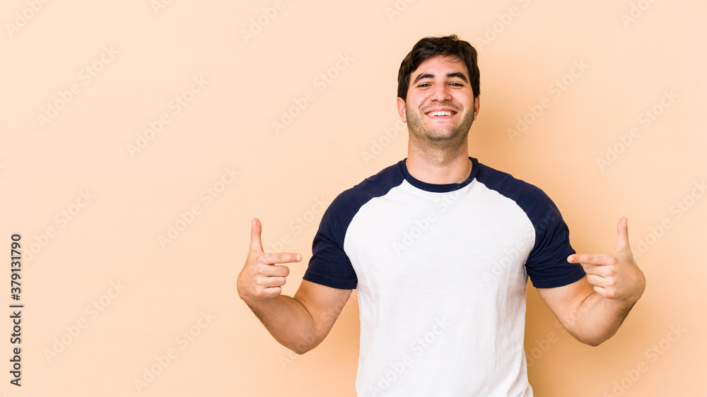 Young man isolated on beige background points down with fingers, positive feeling. Young man isolated on beige background points down with fingers, positive feeling.