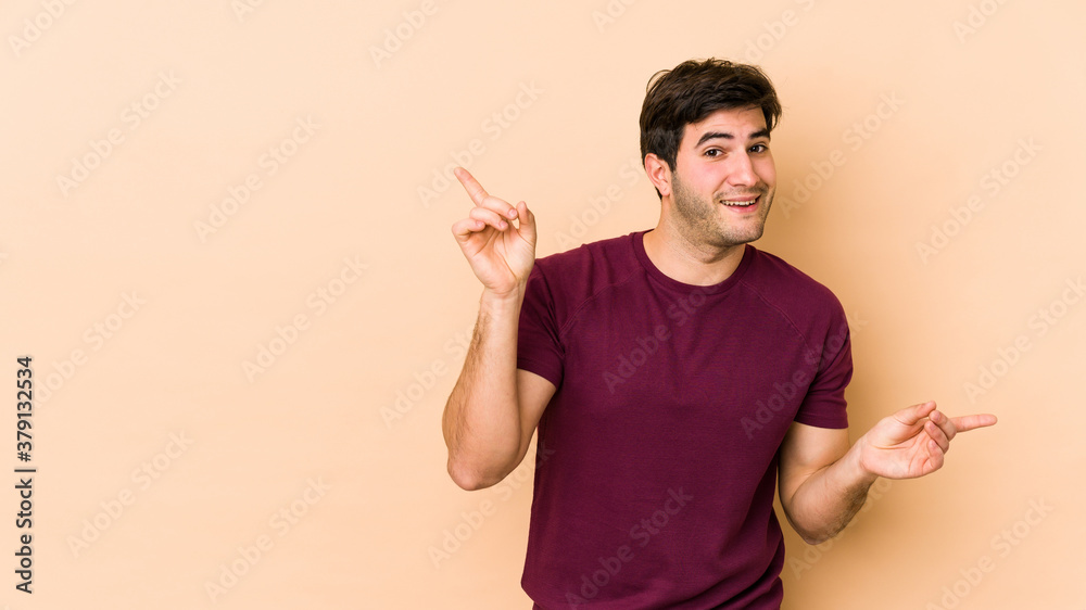 Young man isolated on beige background pointing to different copy spaces, choosing one of them, showing with finger. Young man isolated on beige background pointing to different copy spaces, choosing one of them, showing with finger.