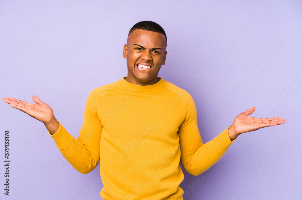 Young latin man isolated on purple background confused and doubtful shrugging shoulders to hold a copy space. Young latin man isolated on purple background confused and doubtful shrugging shoulders to hold a copy space.