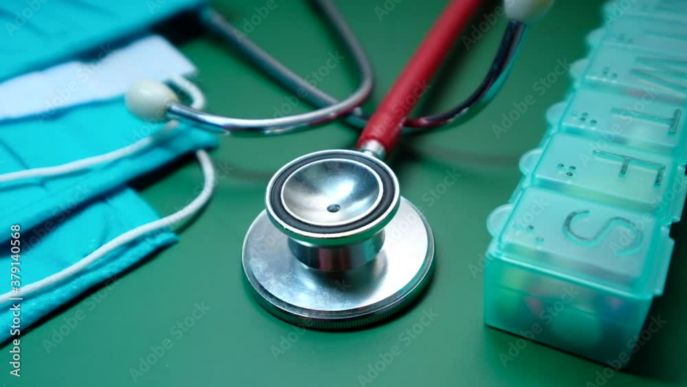 Close up of stethoscope, mask and pill box on green background Close up of stethoscope, mask and pill box on green background