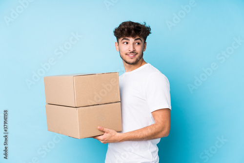Young arab man holding boxes isolated looks aside smiling, cheerful and pleasant.