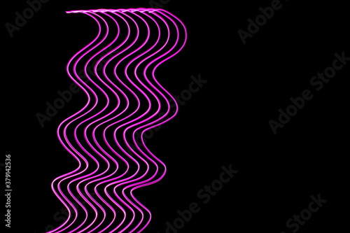 Long exposure photograph of neon pink colour in an abstract swirl  parallel lines pattern against a black background. Light painting photography.