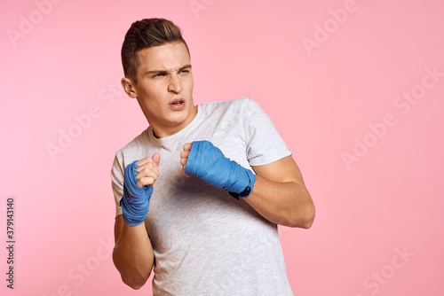 Guy in blue gloves on a pink background are boxing in a white t-shirt cropped view