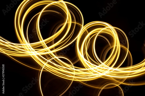 Long exposure photograph of neon gold colour in an abstract swirl, parallel lines pattern against a black background. Light painting photography.