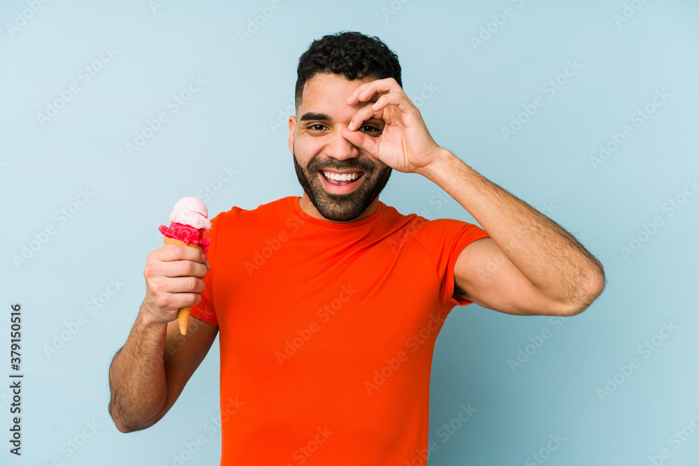 Young latin man holding an ice cream isolated excited keeping ok gesture on eye. Young latin man holding an ice cream isolated excited keeping ok gesture on eye.
