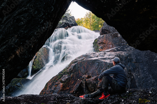 Man in the cave with waterfall i the background.