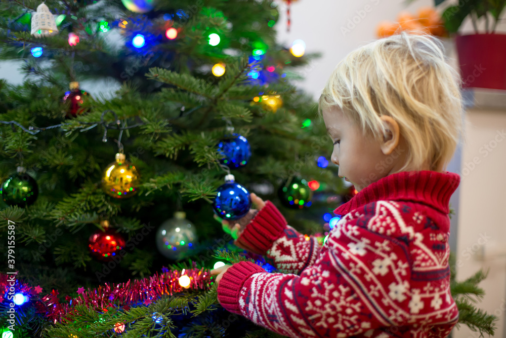 Cute little blonde boy with Christmas sweater, decorating christmas tree