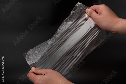 Two hands are testing the toughness of transparent plastic bags against a black background
